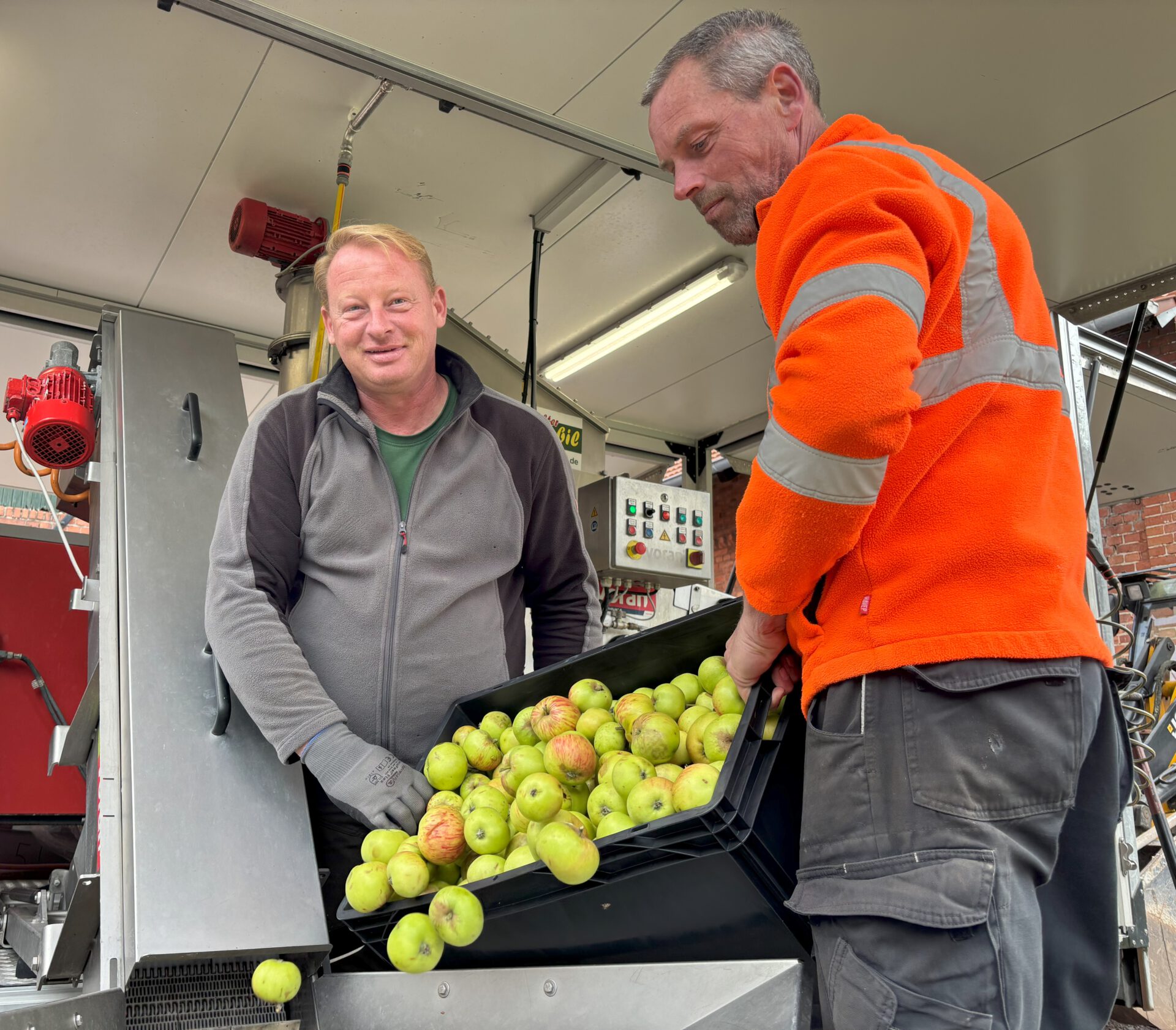Sebastian Twele (Obstgehölzpflege Twele in Frille; rechts) und Lutz Wege (Saftmobil Uchte) mit angelieferten Äpfeln, die in kurzer Zeit zu Saft gemacht werden. Foto: Jessica Höffner