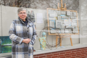 Künstlerin Margit Birkenhauer vor dem Schaufenster des Petershäger Anzeigers, in dem derzeit ihre Arbeiten – darunter die Collage „Menschenrechte“ – zu sehen sind. Foto: Krischi Meier